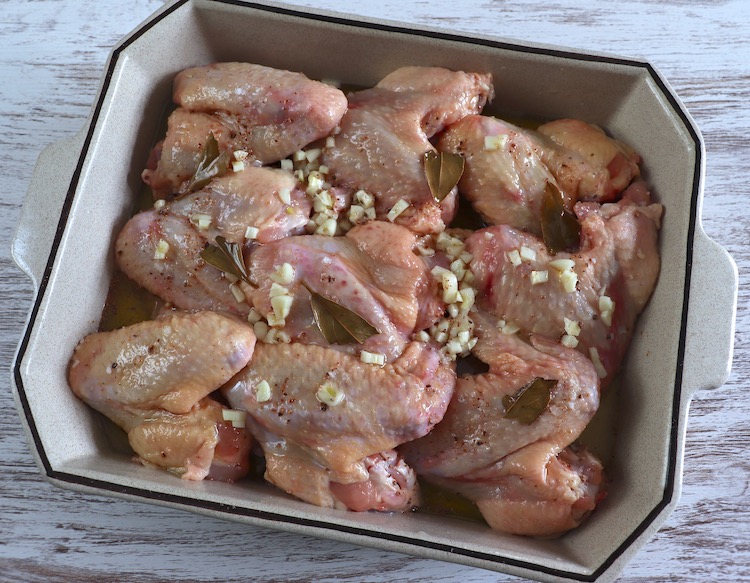 Chicken wings seasoned with salt, chopped garlic, nutmeg, olive oil, lemon juice and bay leaf on a baking dish