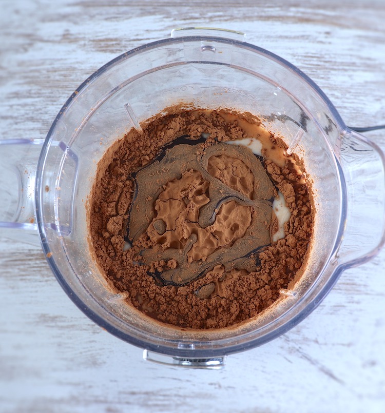 Cocoa powder, chocolate chips, chocolate syrup, yogurt and sugar on a blender