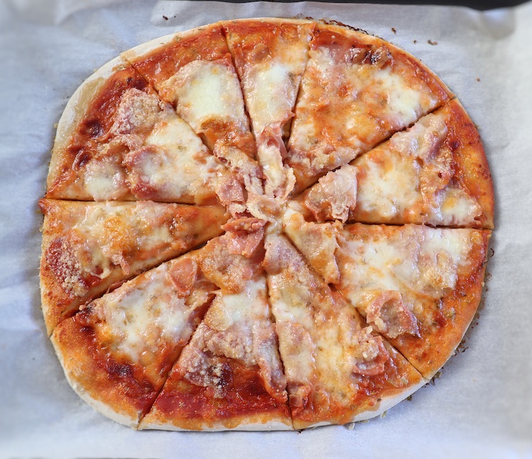Pizza de presunto e queijo num tabuleiro forrado com papel vegetal