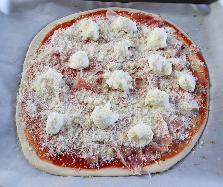 Massa de pizza com presunto, queijo, polpa de tomate e orégãos num tabuleiro forrado com papel vegetal