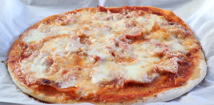 Pizza de presunto e queijo num tabuleiro forrado com papel vegetal