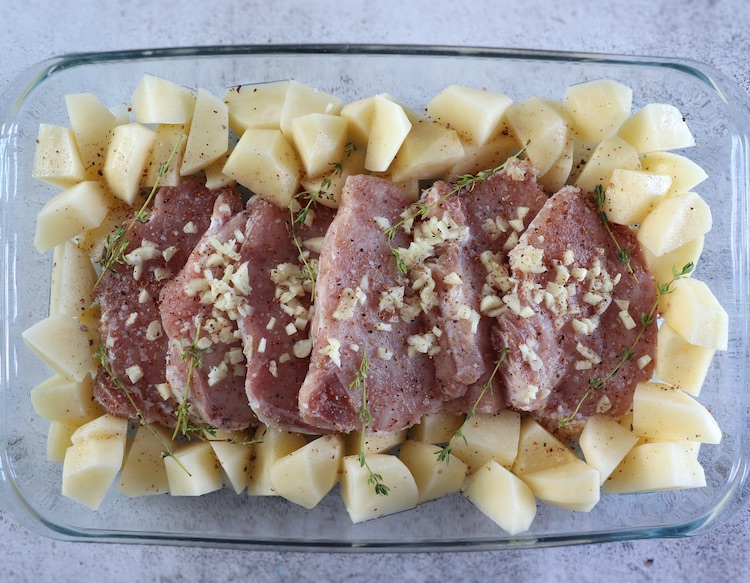 Pork loin slices and potatoes seasoned with salt, nutmeg, pepper, chopped garlic, thyme and sliced onion on a baking dish
