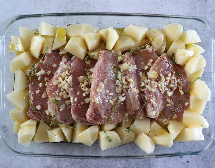 Pork loin slices and potatoes seasoned with salt, nutmeg, pepper, chopped garlic, thyme, sliced onion, olive oil and white wine on a baking dish