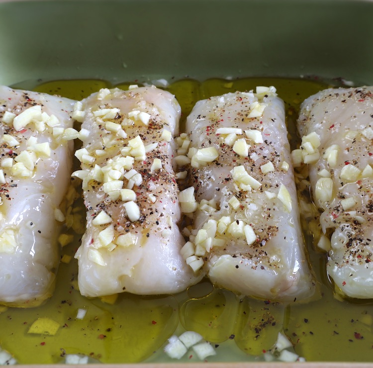 Hake loins seasoned with lemon juice, salt, pepper, chopped garlic and olive oil in a baking dish